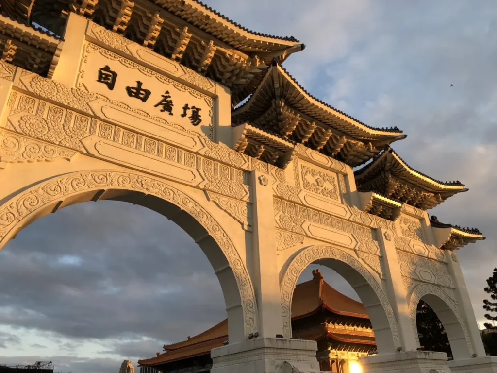 A photo of the entrance gate to the Chiang Kai Shek Memorial Hall in Taipei, Taiwan. The gate is grand and imposing, with tall white columns and a red roof.